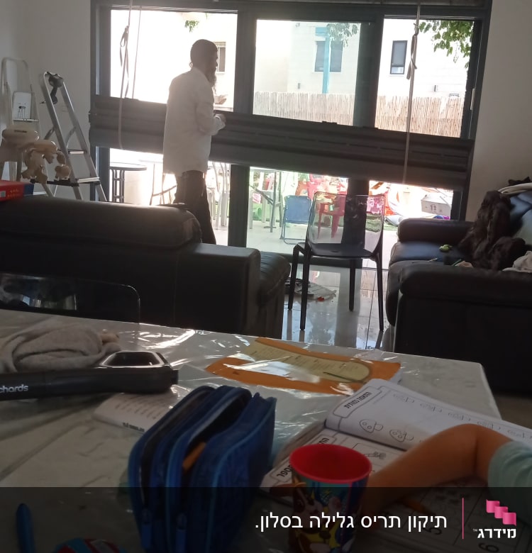 אדם מתקין תריסים בחלון גדול בסלון